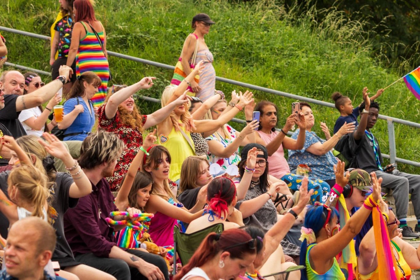 A diverse crowd joyfully celebrating with raised hands at a pride event.