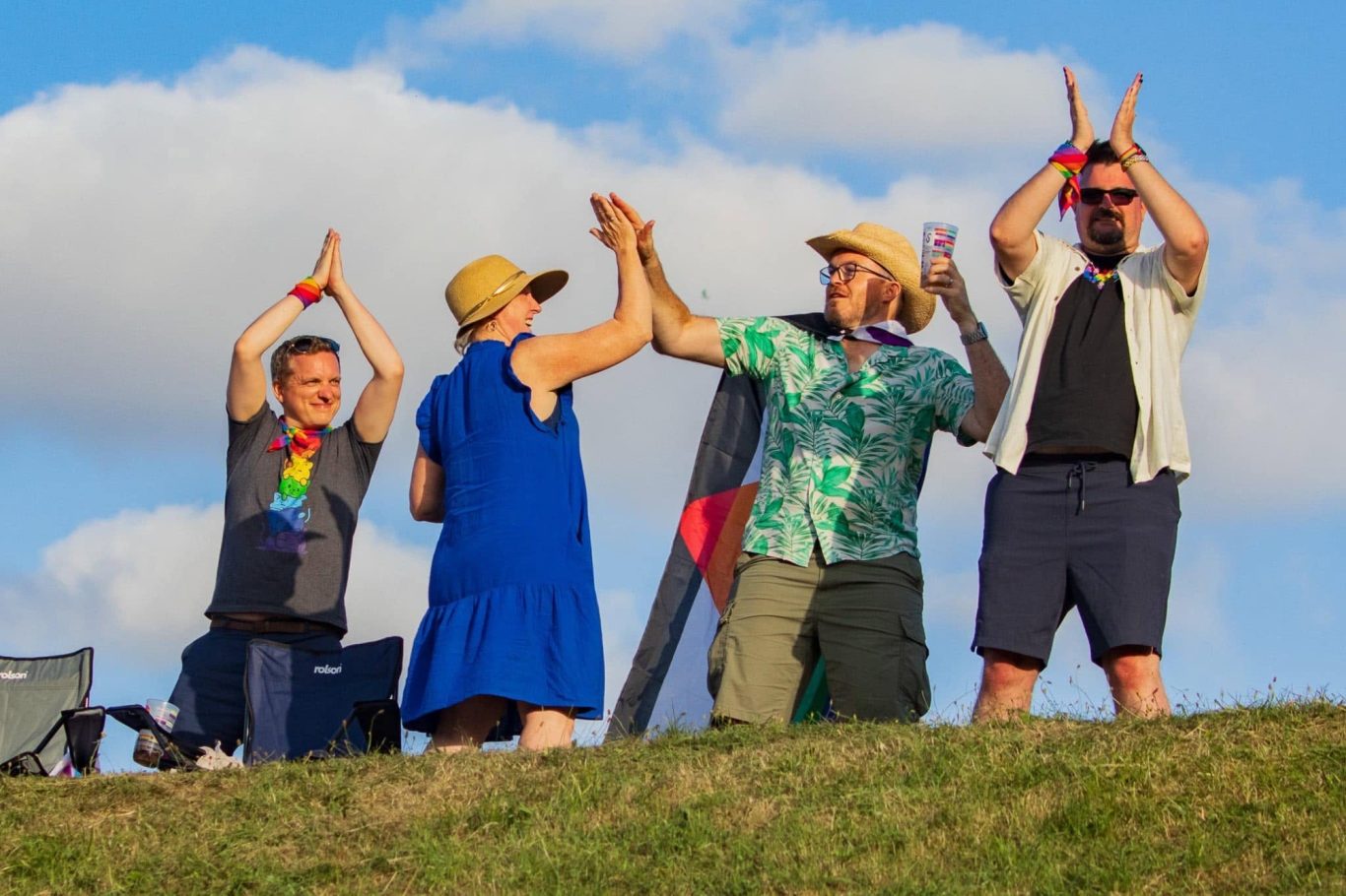 A group of people celebrating outdoors, raising their hands against a bright blue sky.