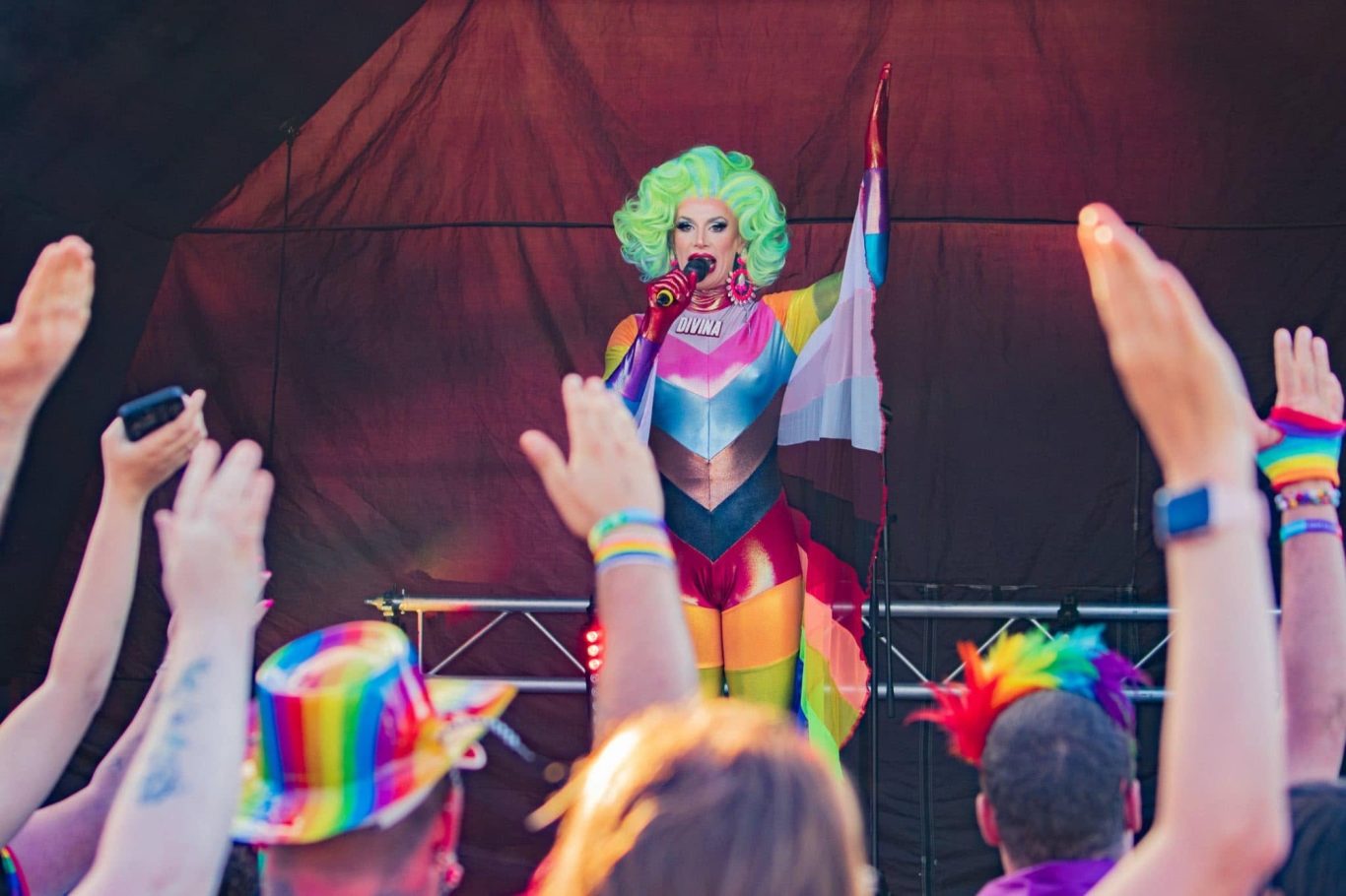 Divina DiCampo - 2024 Drag performer with green hair sings on stage, surrounded by a vibrant crowd celebrating Pride.