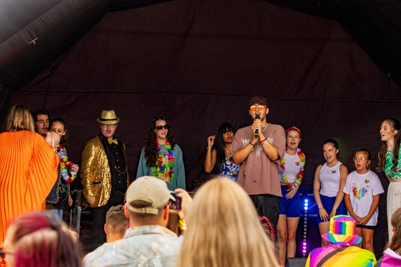 GYG - 2024 A group of people on stage during a lively event, wearing colourful outfits and accessories.
