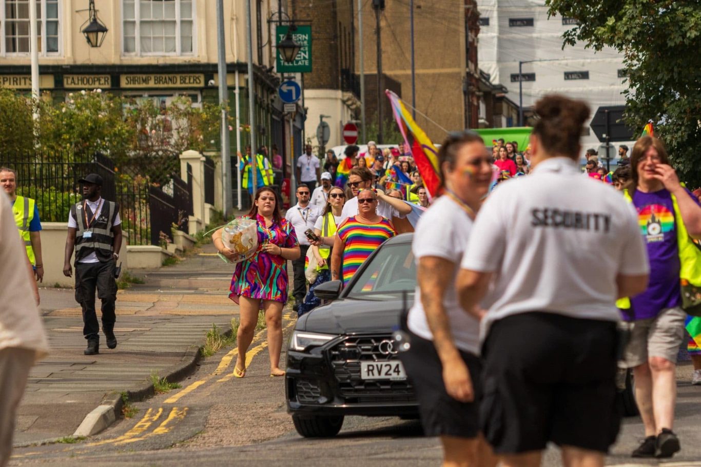 A lively street scene with people celebrating in rainbow attire during a parade.