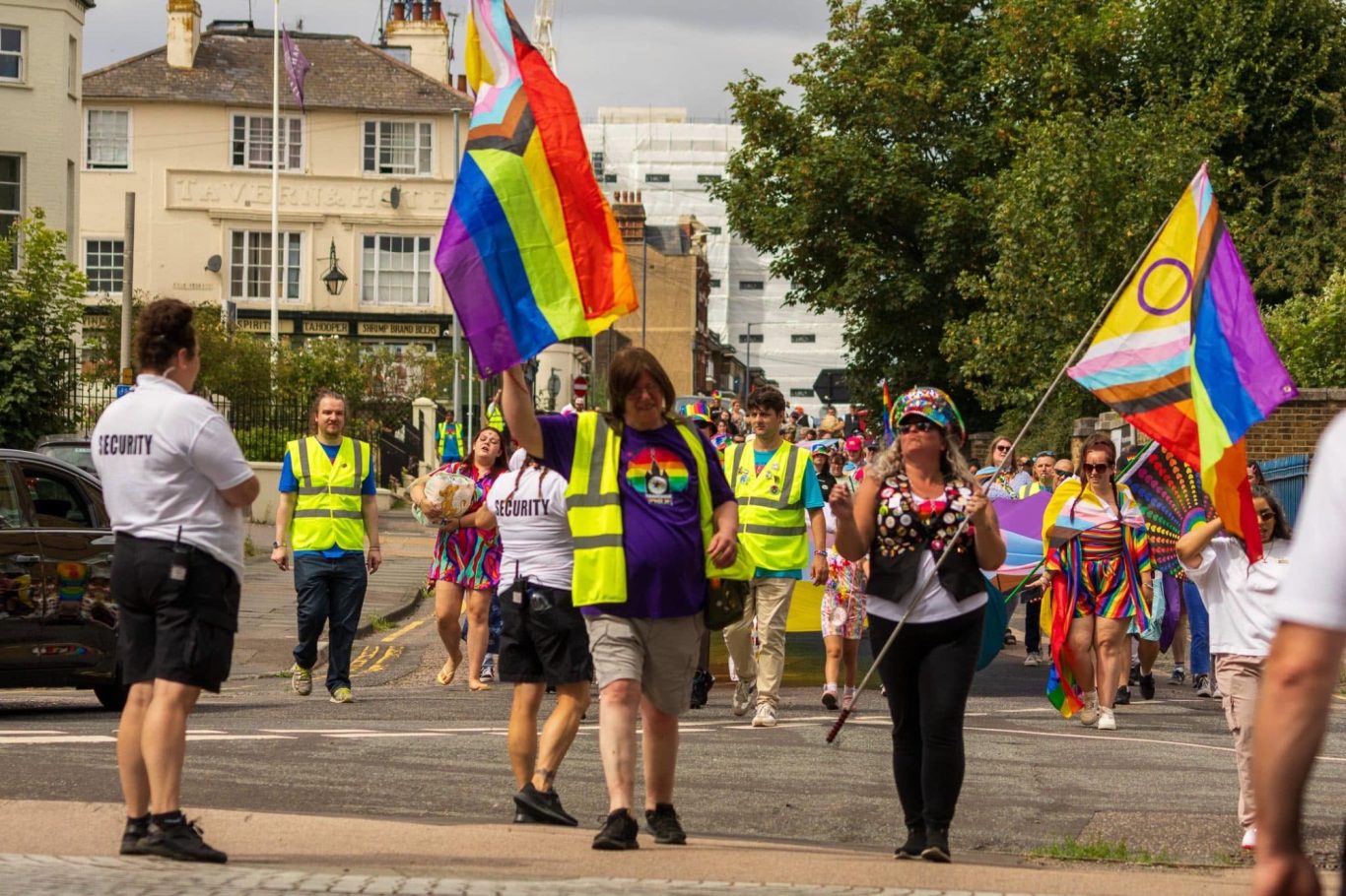 A lively parade with people holding rainbow flags and wearing colourful attire.