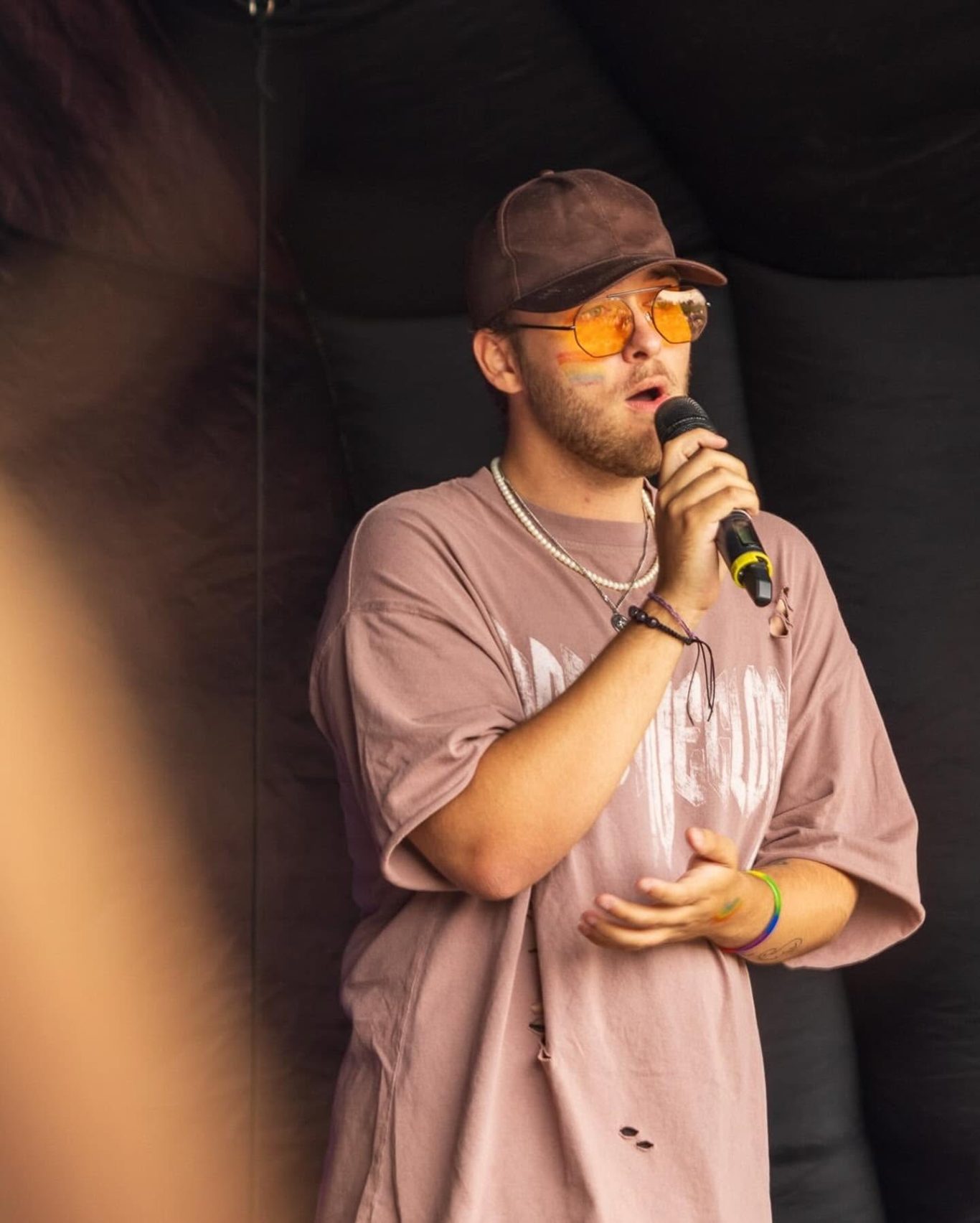 GYG - 2024 Man singing into a microphone, wearing a brown cap and orange sunglasses.