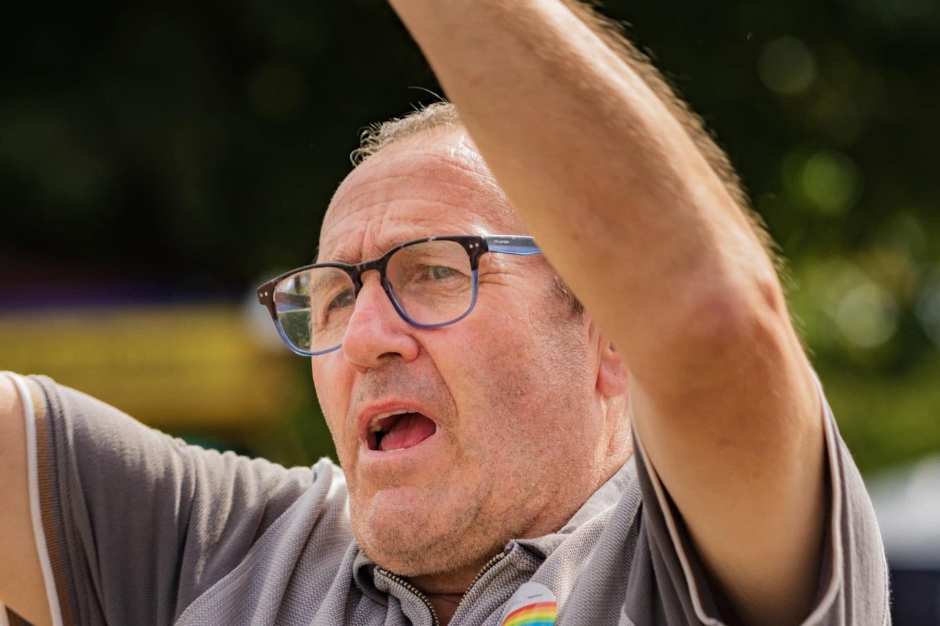 A man with glasses raising his arms, displaying a focused expression outdoors.