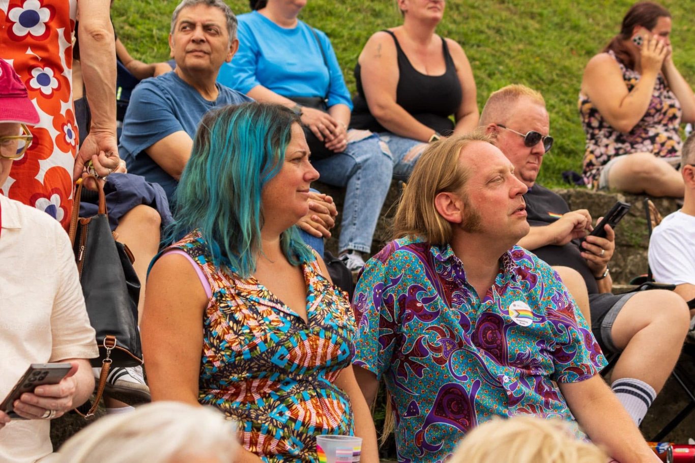 Two people sitting among a crowd, both looking attentively at something off-screen.