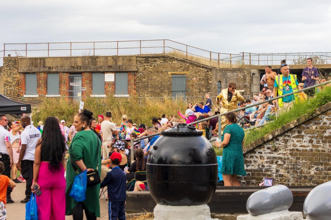 A crowded outdoor event with people gathered by a stone wall and steps.