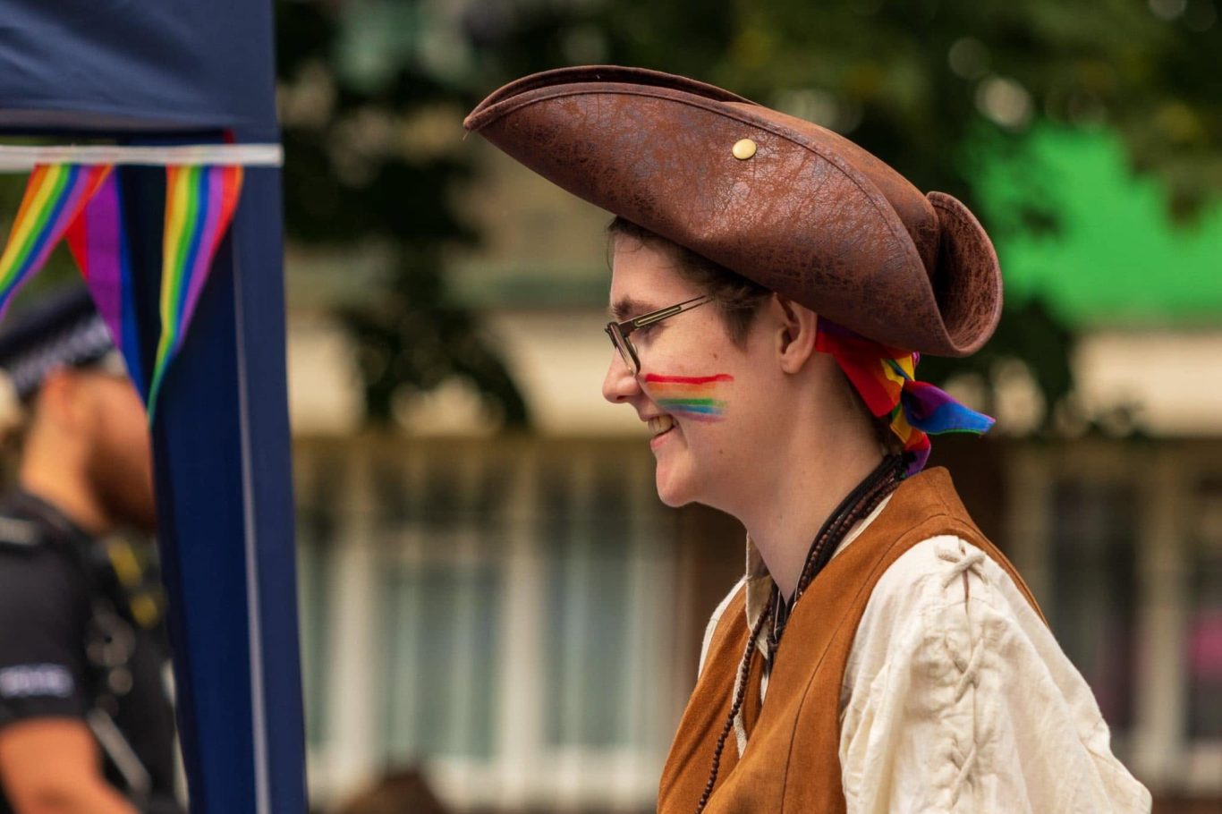 Person wearing a pirate hat and rainbow-themed face paint, smiling.