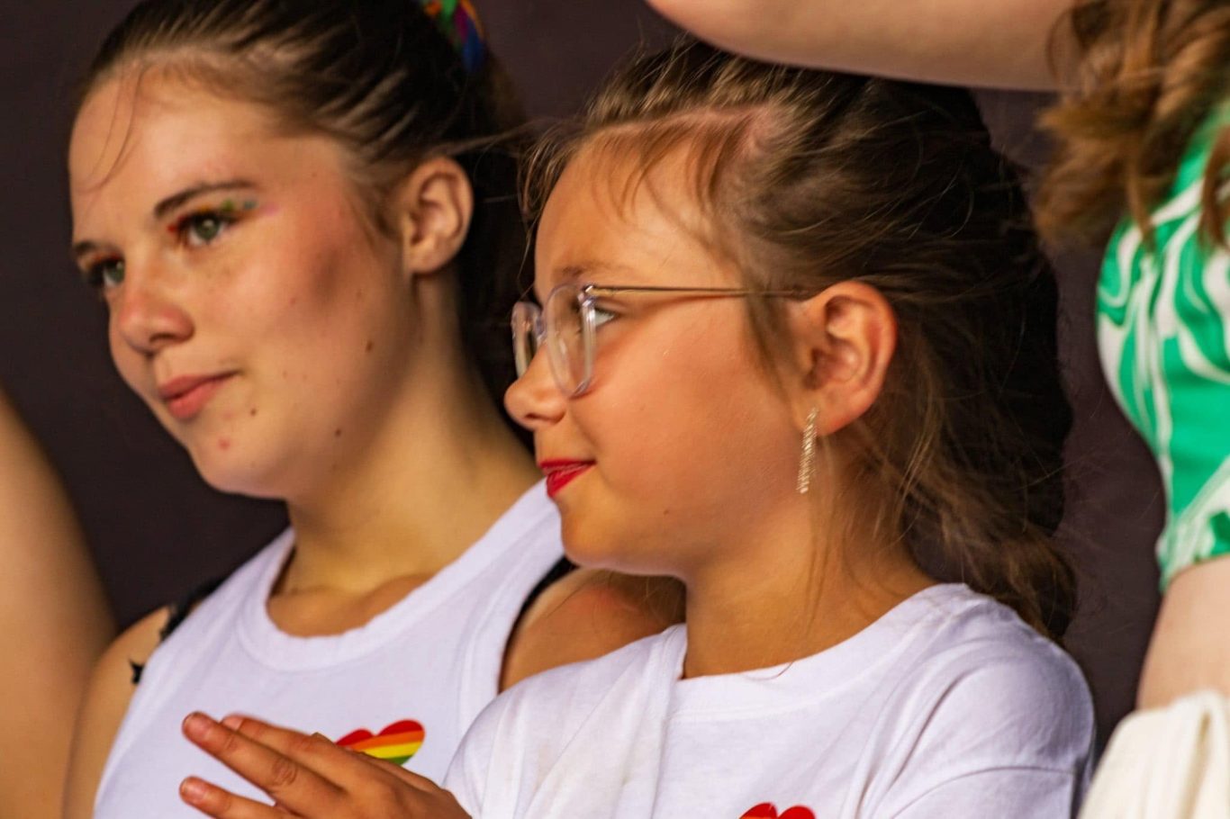Two young girls, one with glasses, smiling and standing together at an event.
