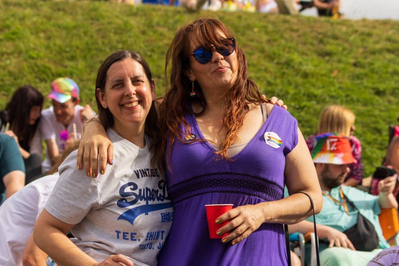 Two women pose together, one in a purple dress and sunglasses, holding a red cup.