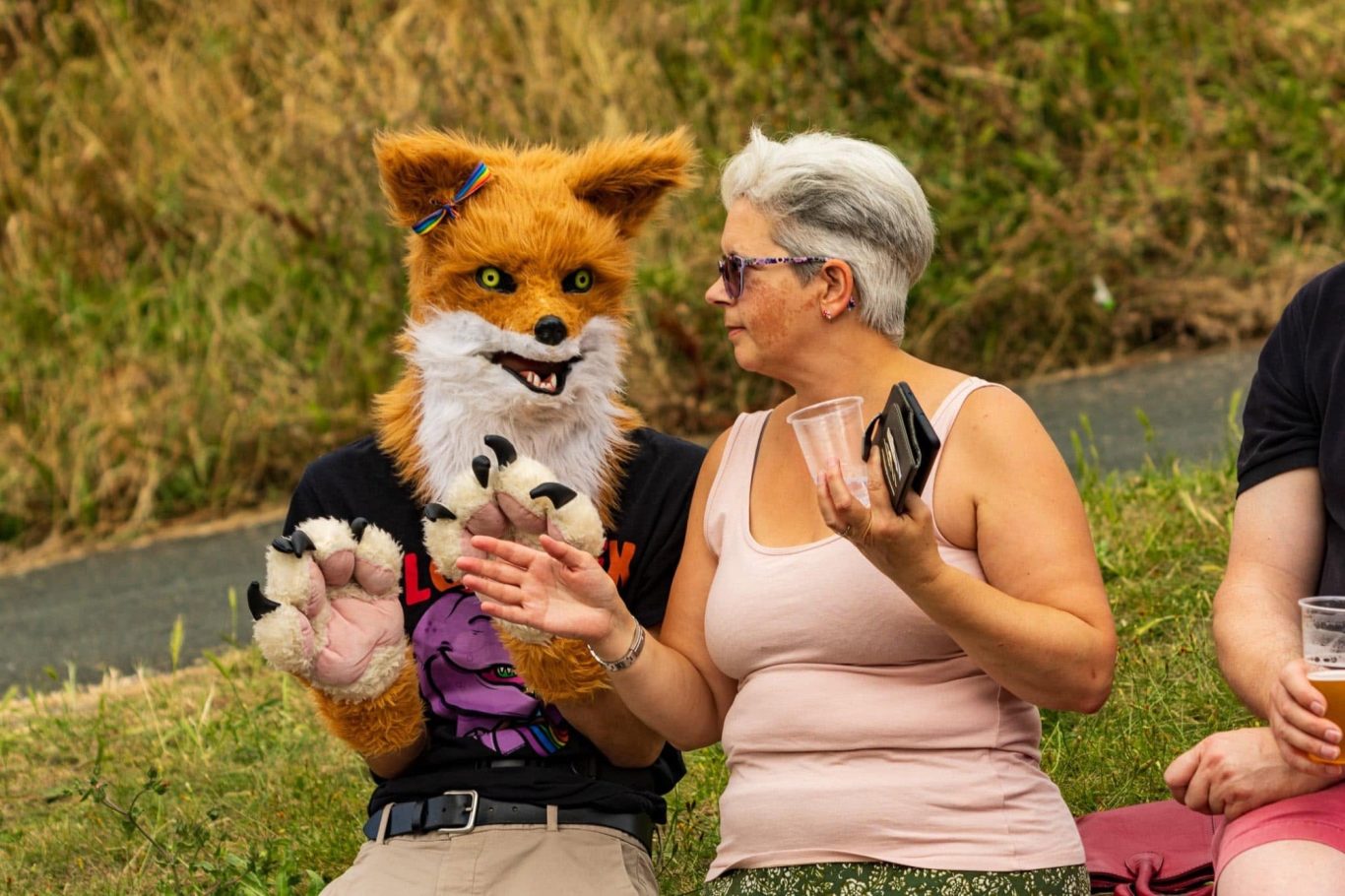 A person in a fox costume talks with a woman outdoors, both smiling and relaxed.