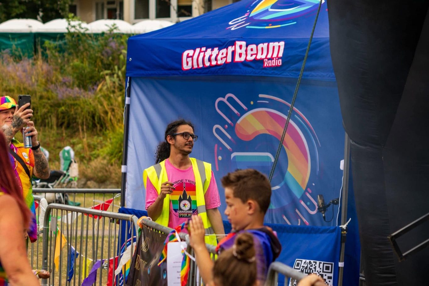 A vibrant festival scene with a booth, a smiling attendee, and rainbow decorations.