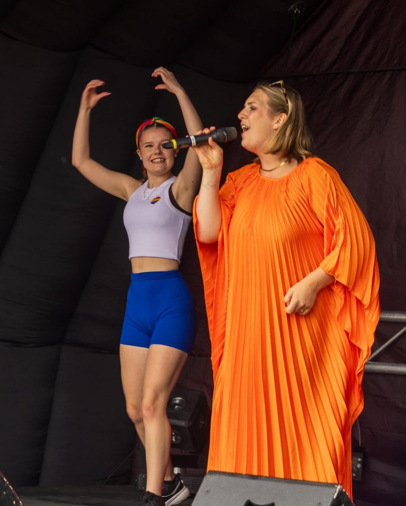 GYG - 2024 Two female performers on stage; one in vibrant orange and the other in sporty attire dancing.