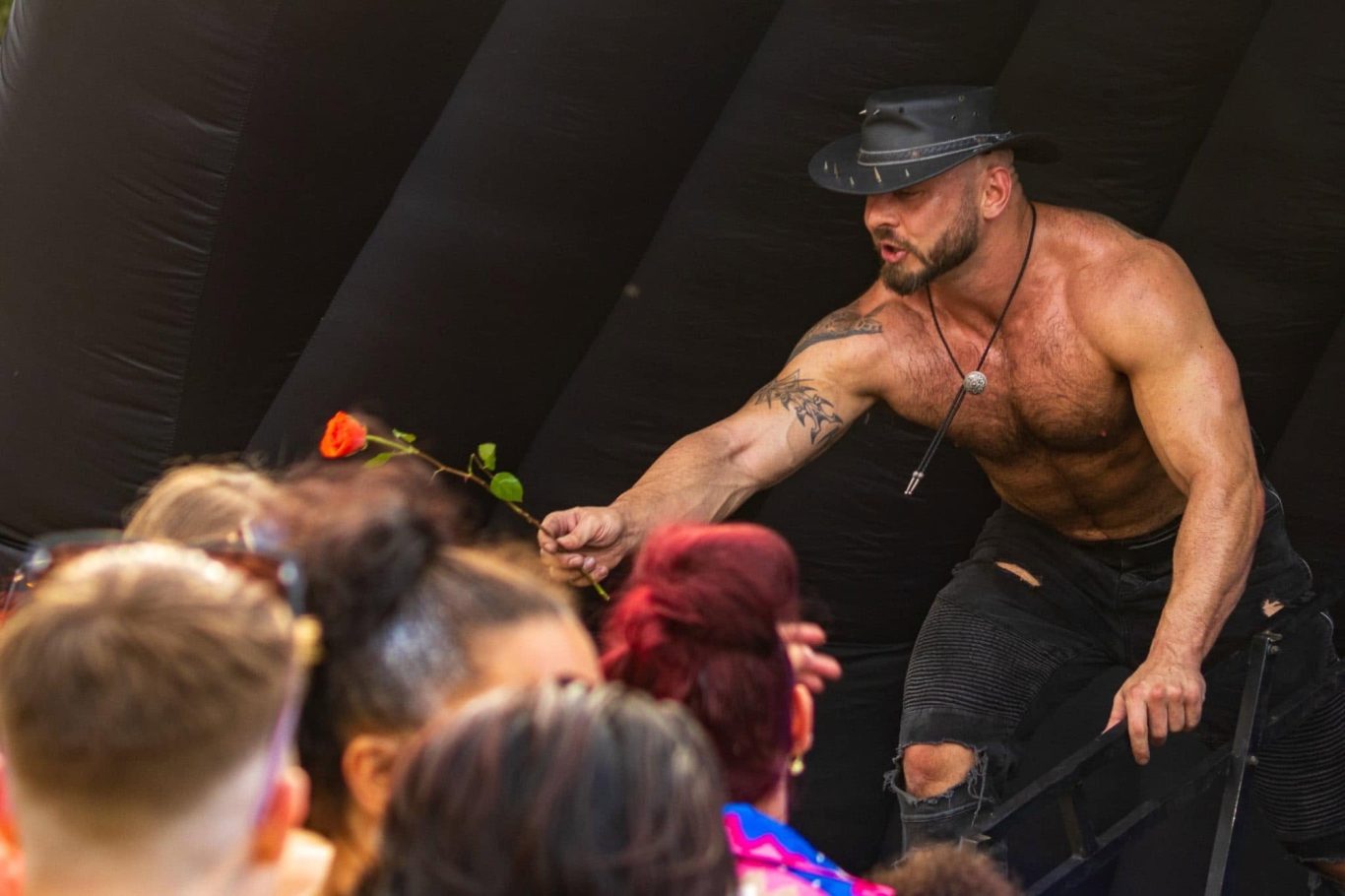Marshall Arkley - 2024 A muscular man in a hat engages with an audience at an outdoor event.