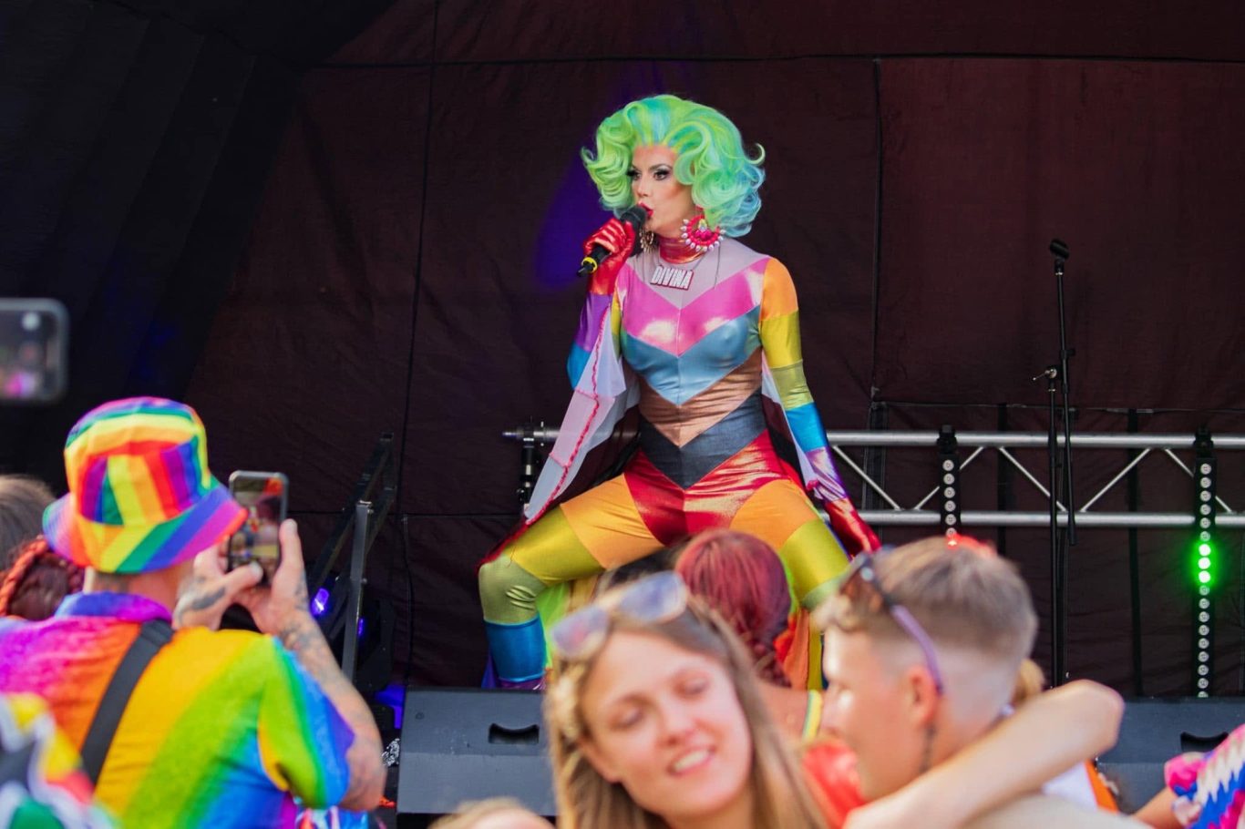 Divina DiCampo - 2024 A performer in vibrant, multicoloured attire entertains a lively, cheering crowd.