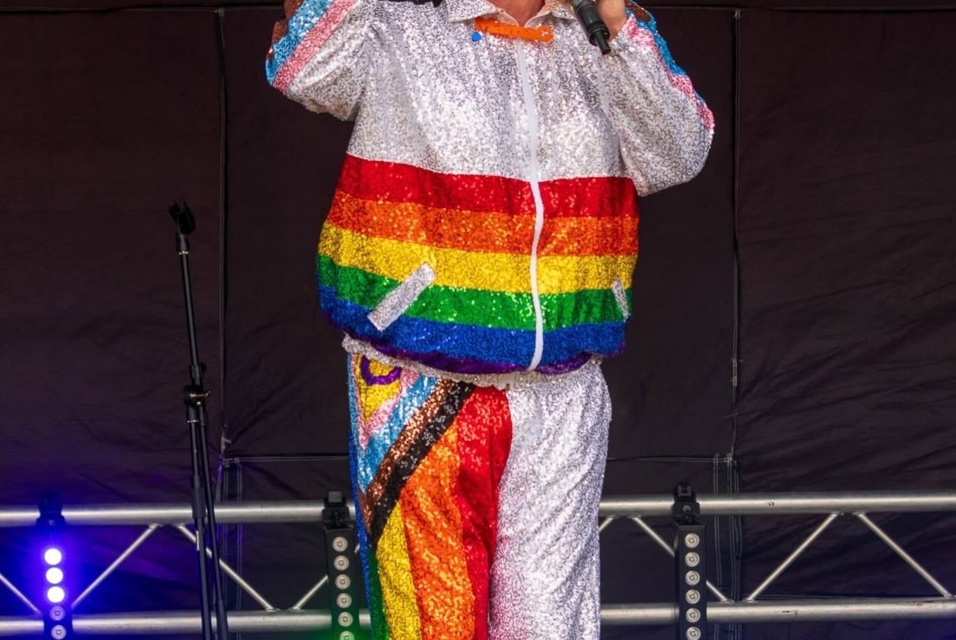 Mama G - 2024 A performer in a rainbow-coloured tracksuit, singing on stage.