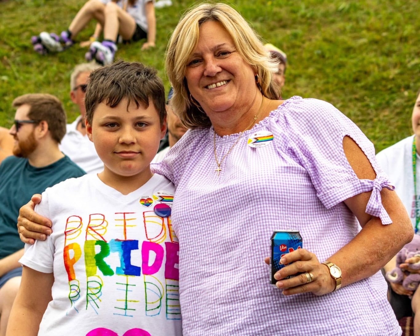 A woman and a boy smile together, both wearing colourful pride-themed attire.