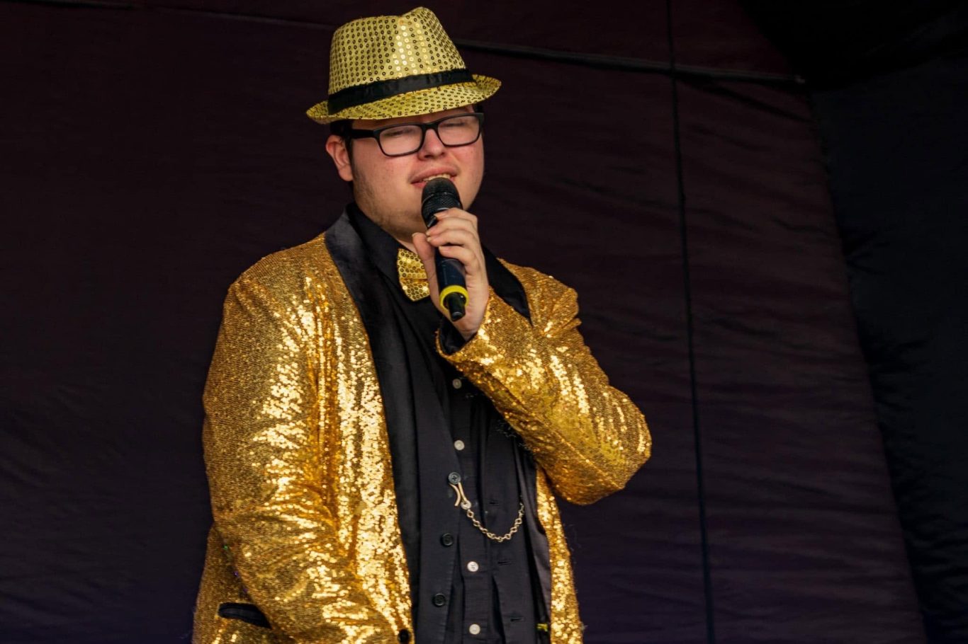 GYG - 2024 Person with glasses wearing a shiny gold suit and hat, singing into a microphone.