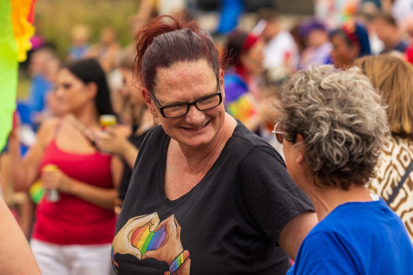 Two women smiling and chatting at a lively outdoor event, surrounded by a diverse crowd.