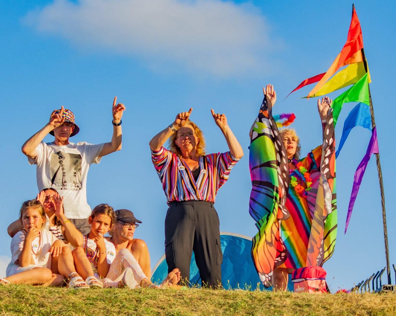 A group of people celebrating with vibrant clothing and a rainbow flag.