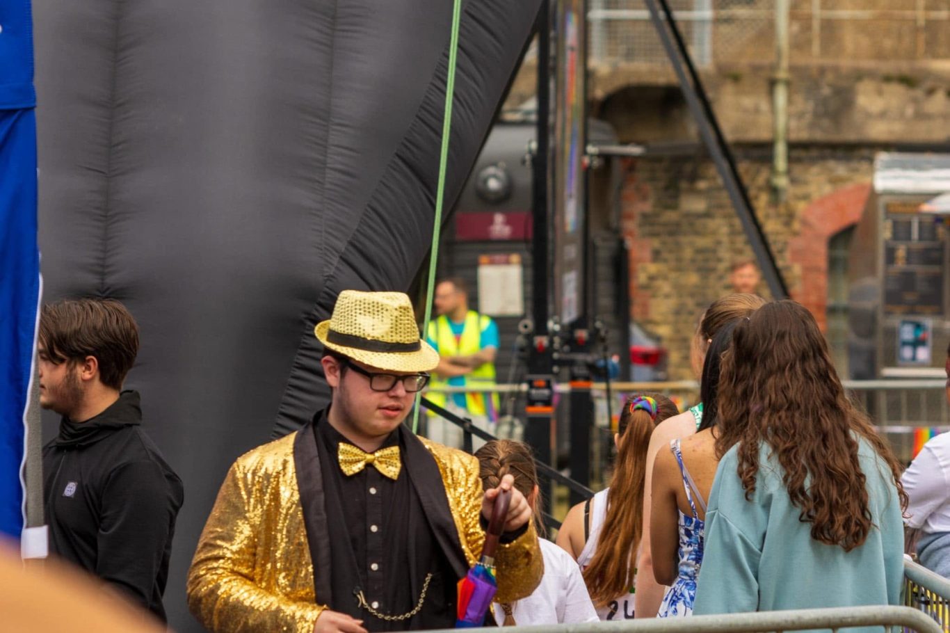 GYG - 2024 Man in a gold suit and hat, holding a microphone at a festive outdoor event.
