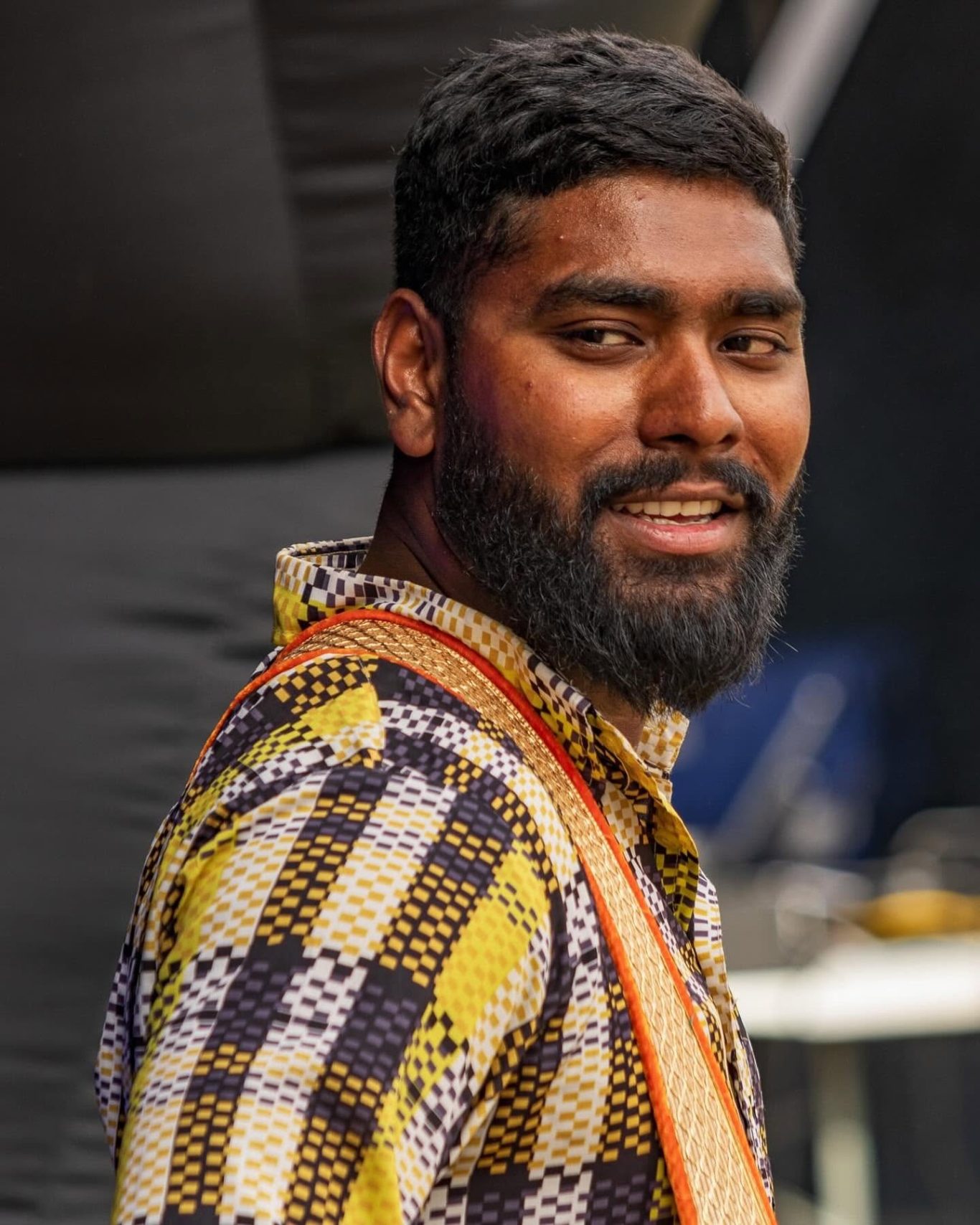 Kings of Dohl Man with a beard, wearing a patterned shirt and an orange safety vest, smiling.