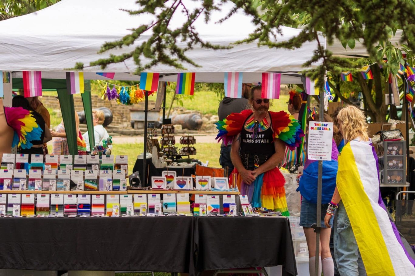Market stall at a pride event, featuring rainbow decorations and colourful merchandise.