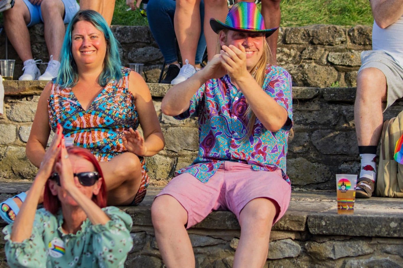 Group of people celebrating, wearing colourful clothing and accessories, outdoors in a festive setting.
