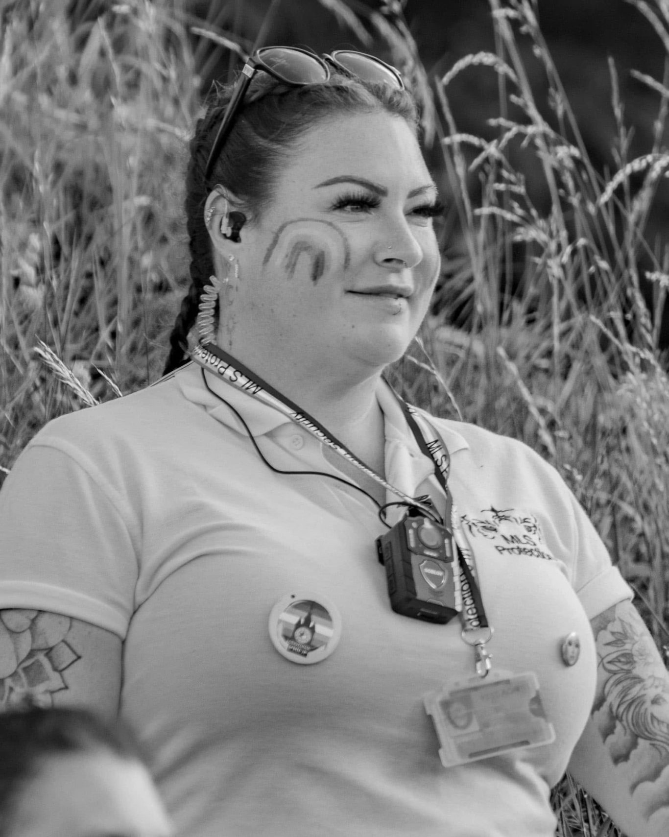 A woman with tattoos wearing a white polo shirt, with a microphone and sunglasses.