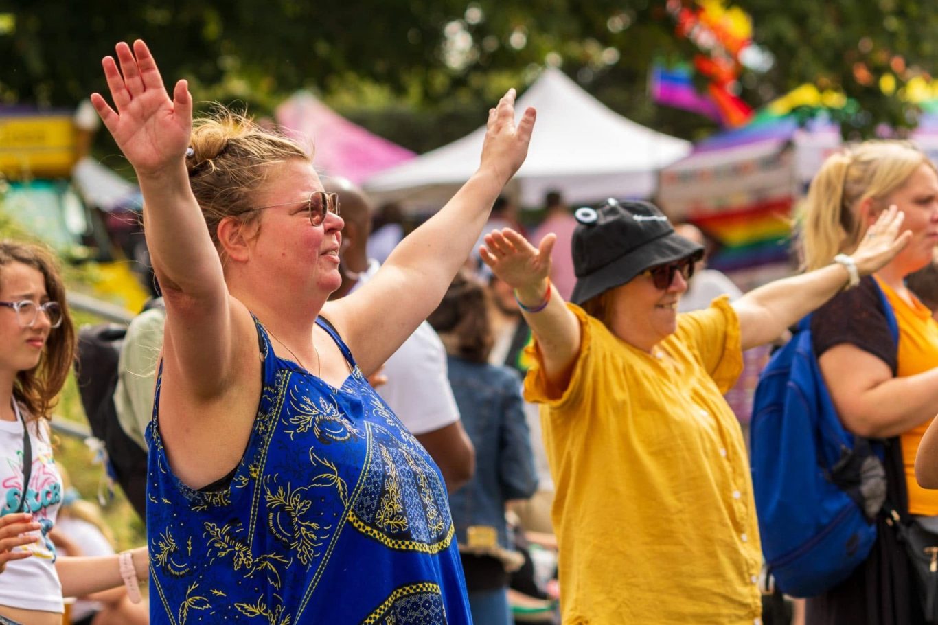 Two women with arms raised enjoying a lively outdoor event, surrounded by a festive crowd.