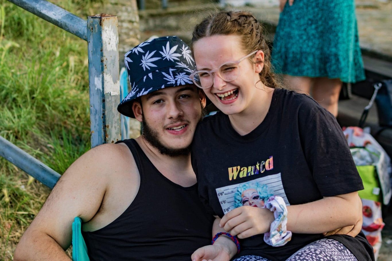 A man and woman laughing together outdoors, sitting on steps with greenery in the background.