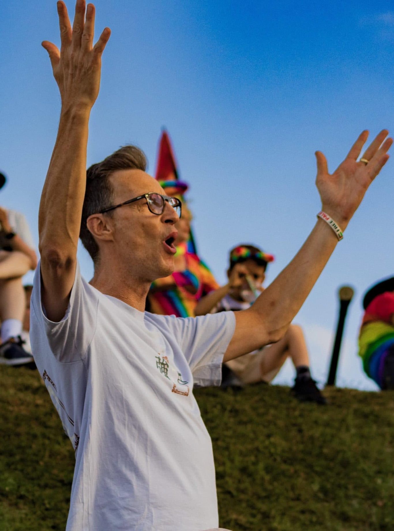 A man passionately speaking with raised hands at a vibrant outdoor event.
