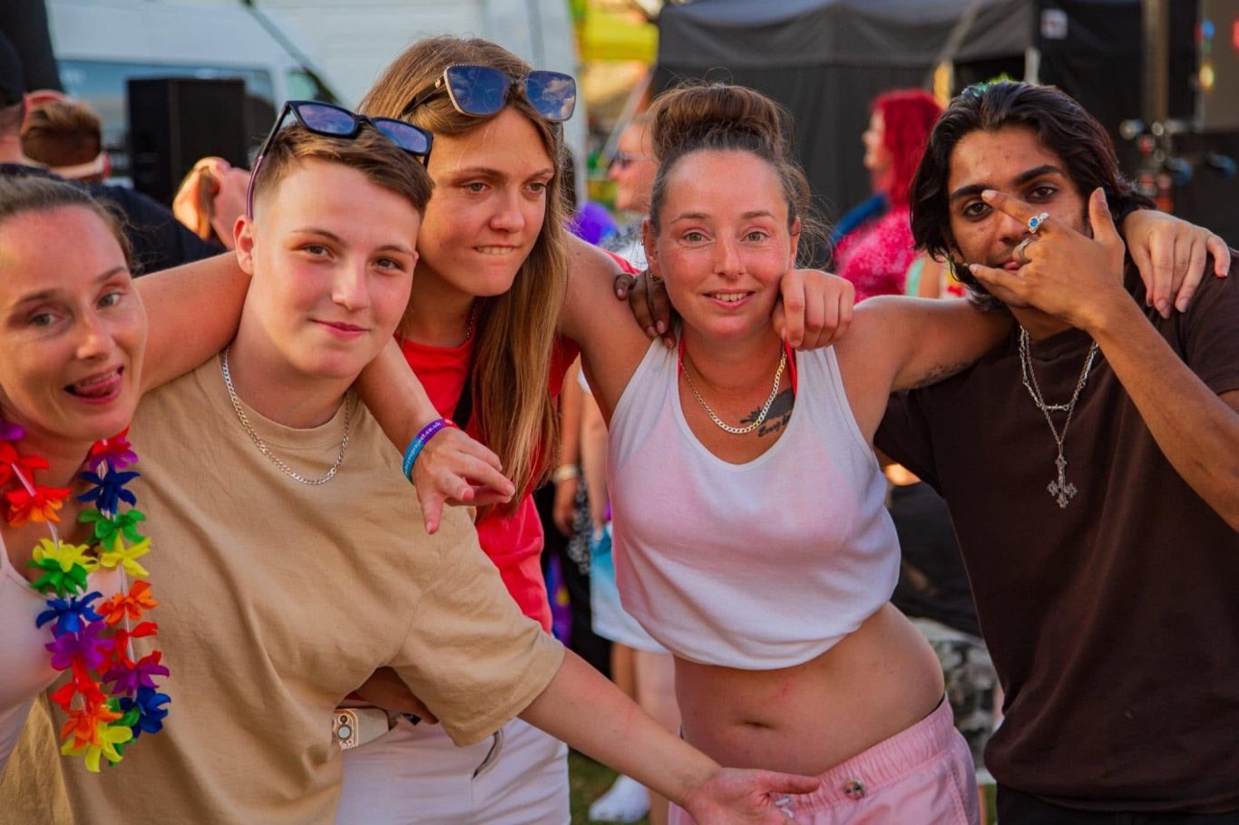 Five friends smiling and posing together at a vibrant outdoor festival.