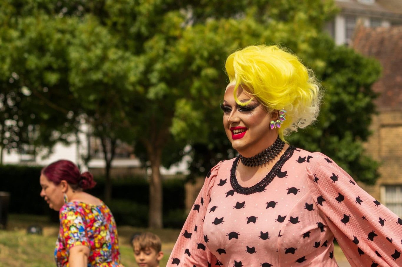 Person in vibrant outfit with yellow hair, smiling, in an outdoor park setting.