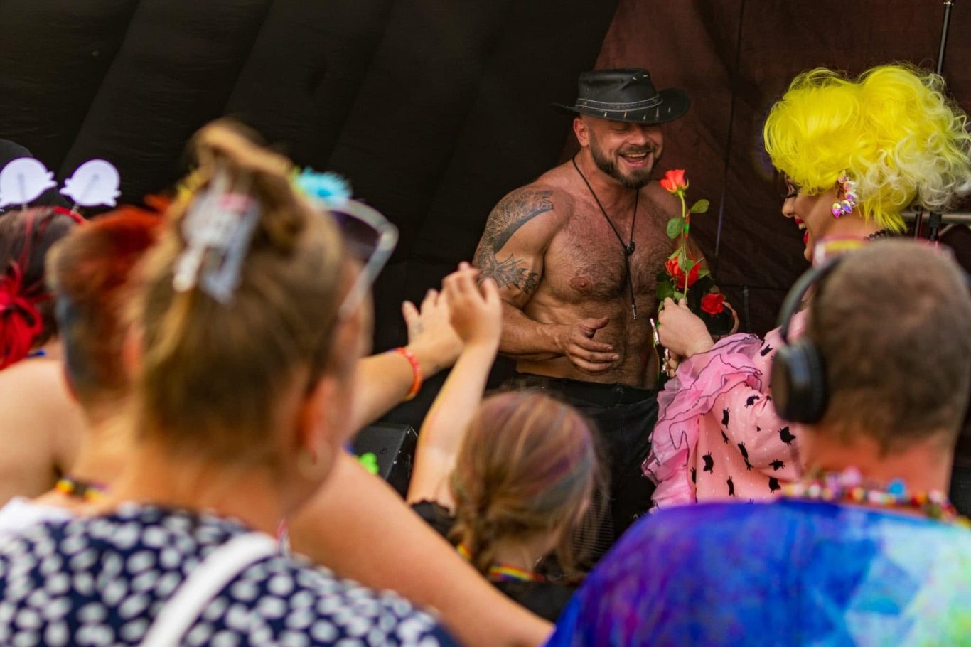 Marshall Arkley - 2024 A muscular performer in a hat receives flowers from a vibrant crowd at a festive event.