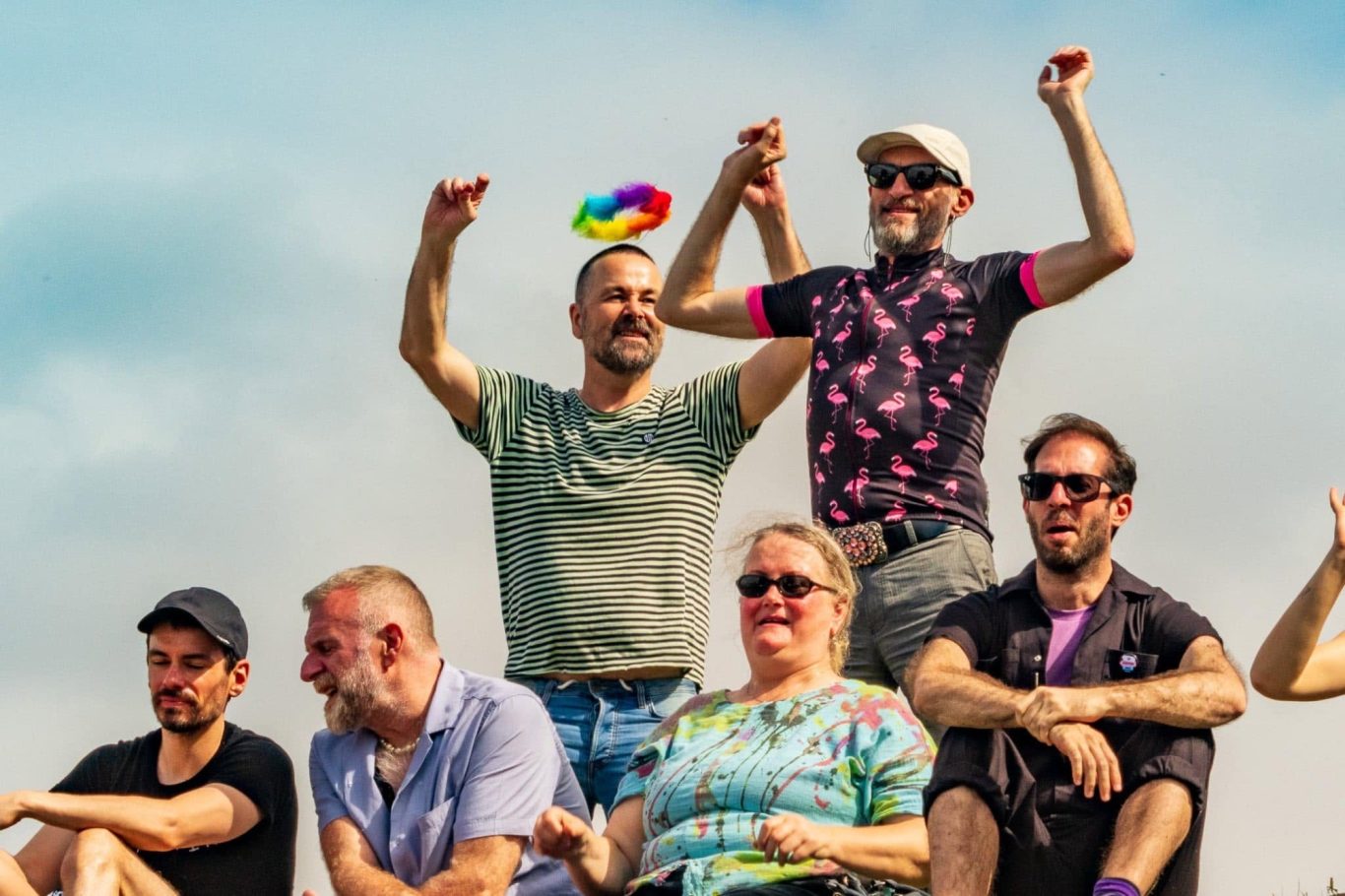 A diverse group of people celebrating, with one person holding a rainbow flag.