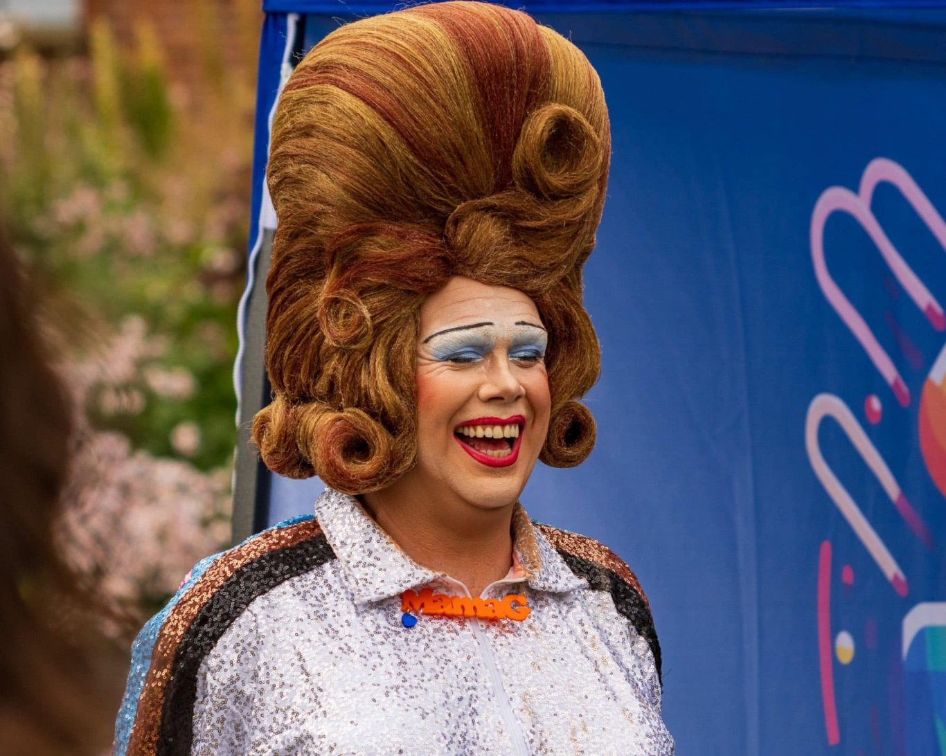 Smiling person in a glittery costume with a large styled hairstyle.