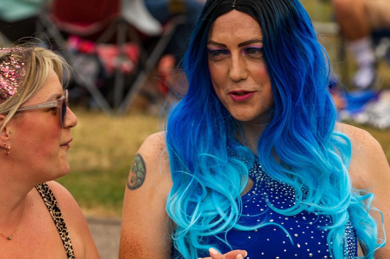 Two people engaged in conversation, one with long blue hair and a sparkly outfit.