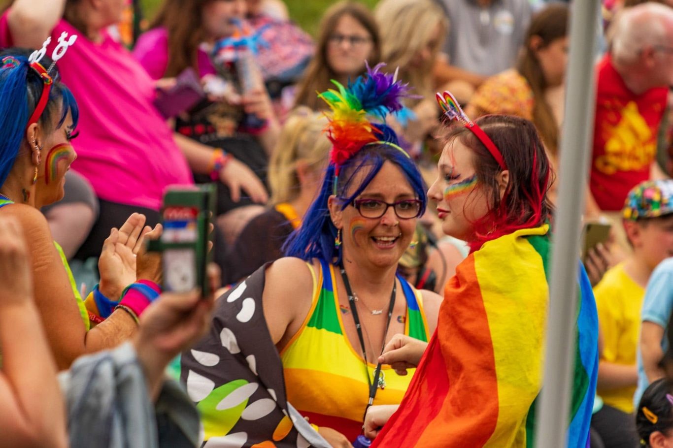 Two people dressed in rainbow colours celebrate at a Pride event, surrounded by other attendees.