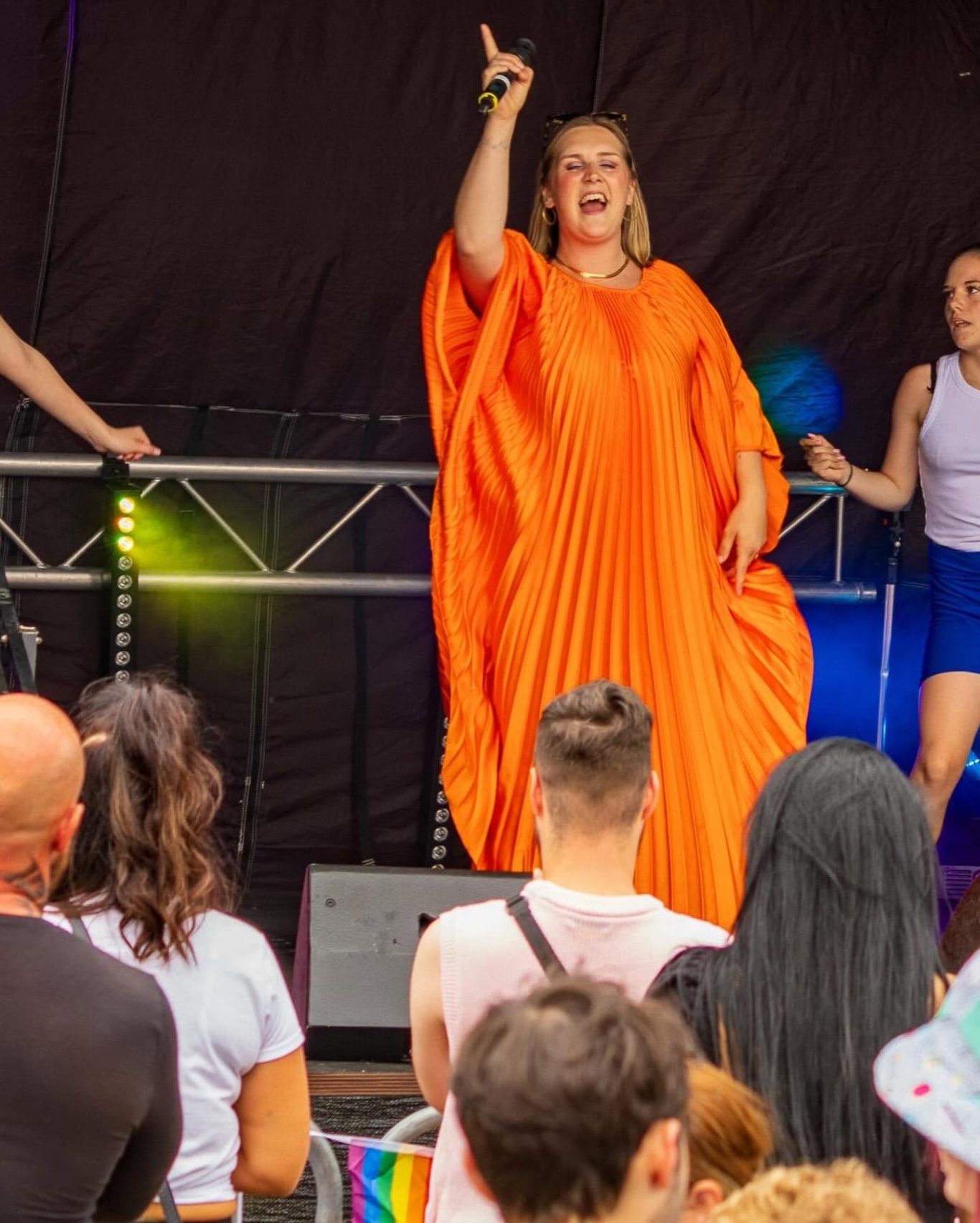 GYG - 2024 A performer in an orange dress sings on stage, entertaining a diverse crowd.